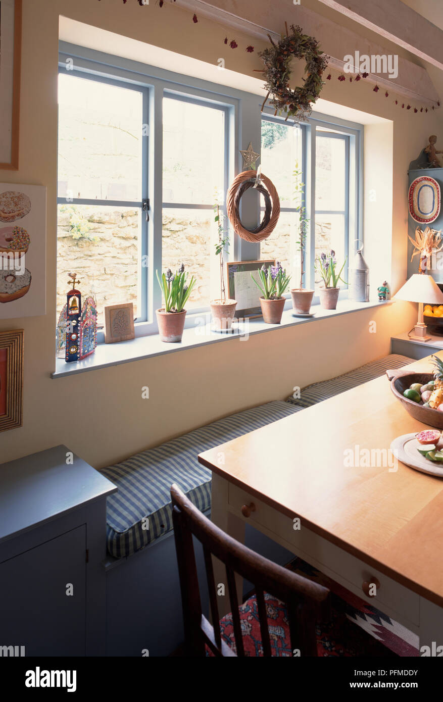 Cucina grande finestra, vasi di fiori fodera davanzale, due corone appeso sopra la finestra del banco, di seguito, lungo tavolo di legno. Foto Stock