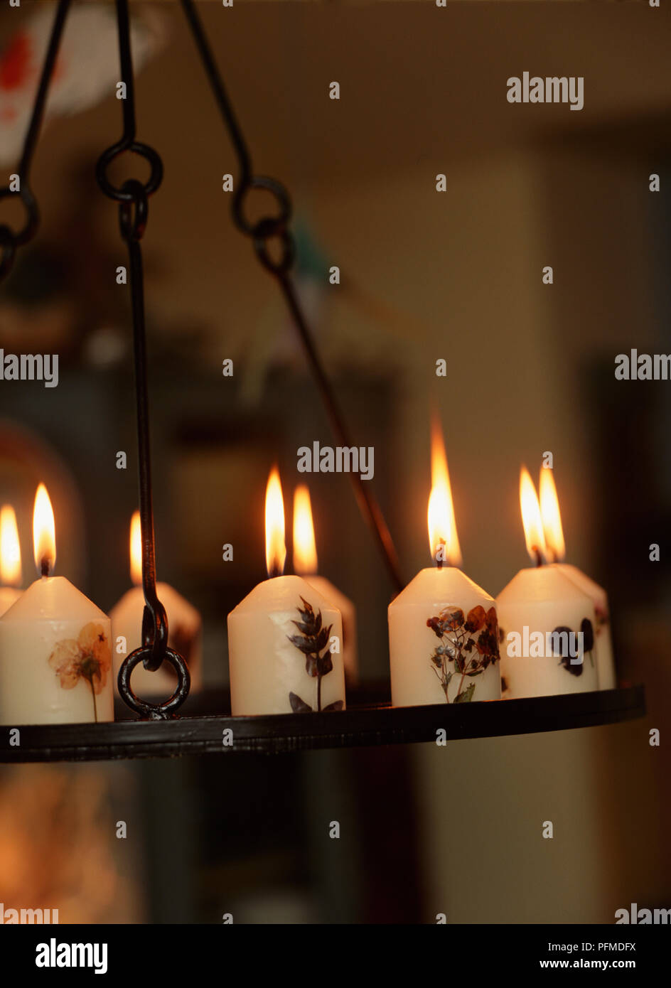 Crema di piccole candele colorate decorate con fiori pressati, fiamme lungo la masterizzazione di stoppini, disposti su appendere la piastra di metallo. Foto Stock