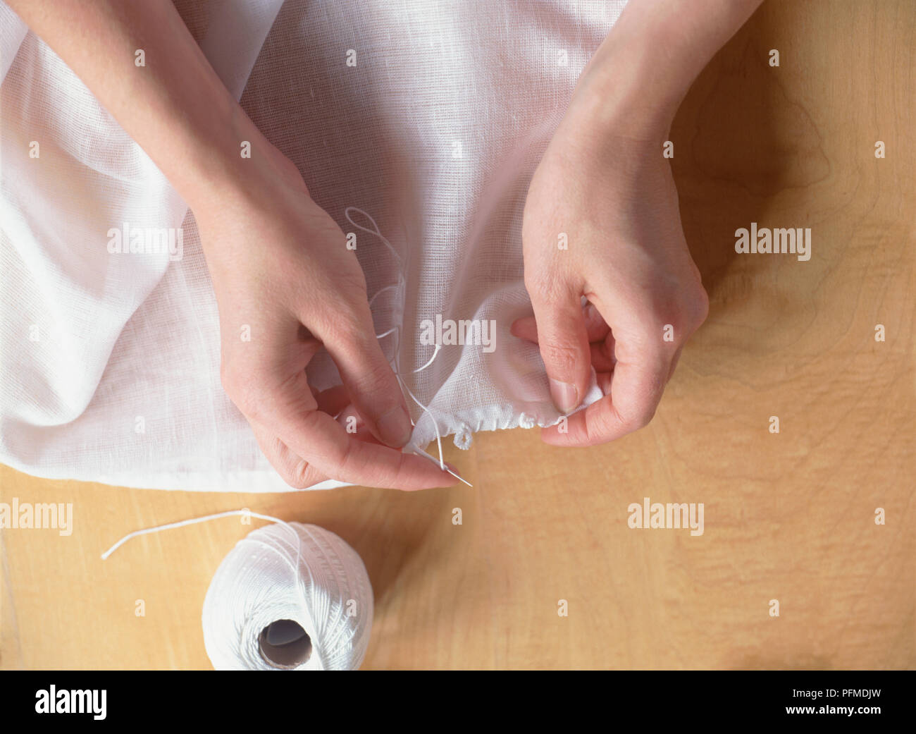 Le mani i bordi da cucire di bianco mussola tenda, filo bianco su maglie, lo stelo di forte cotone bianco di vista di cui sopra. Foto Stock