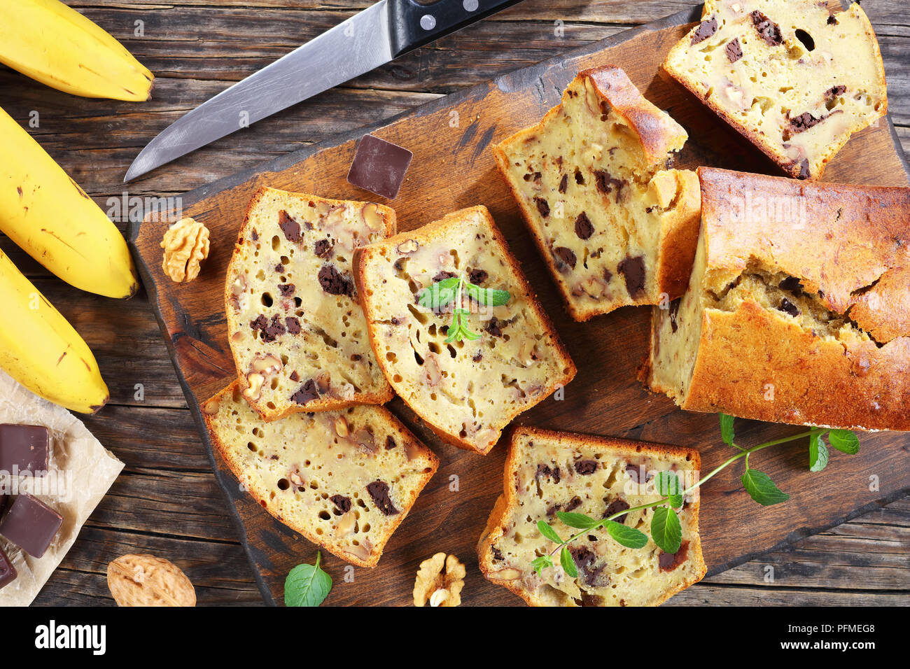 Pane appena sfornato delizioso pane alla banana con noci e cioccolato di pezzi tagliati in fettine su tagliere. ingredienti e coltello su scuri in legno rustico tab Foto Stock