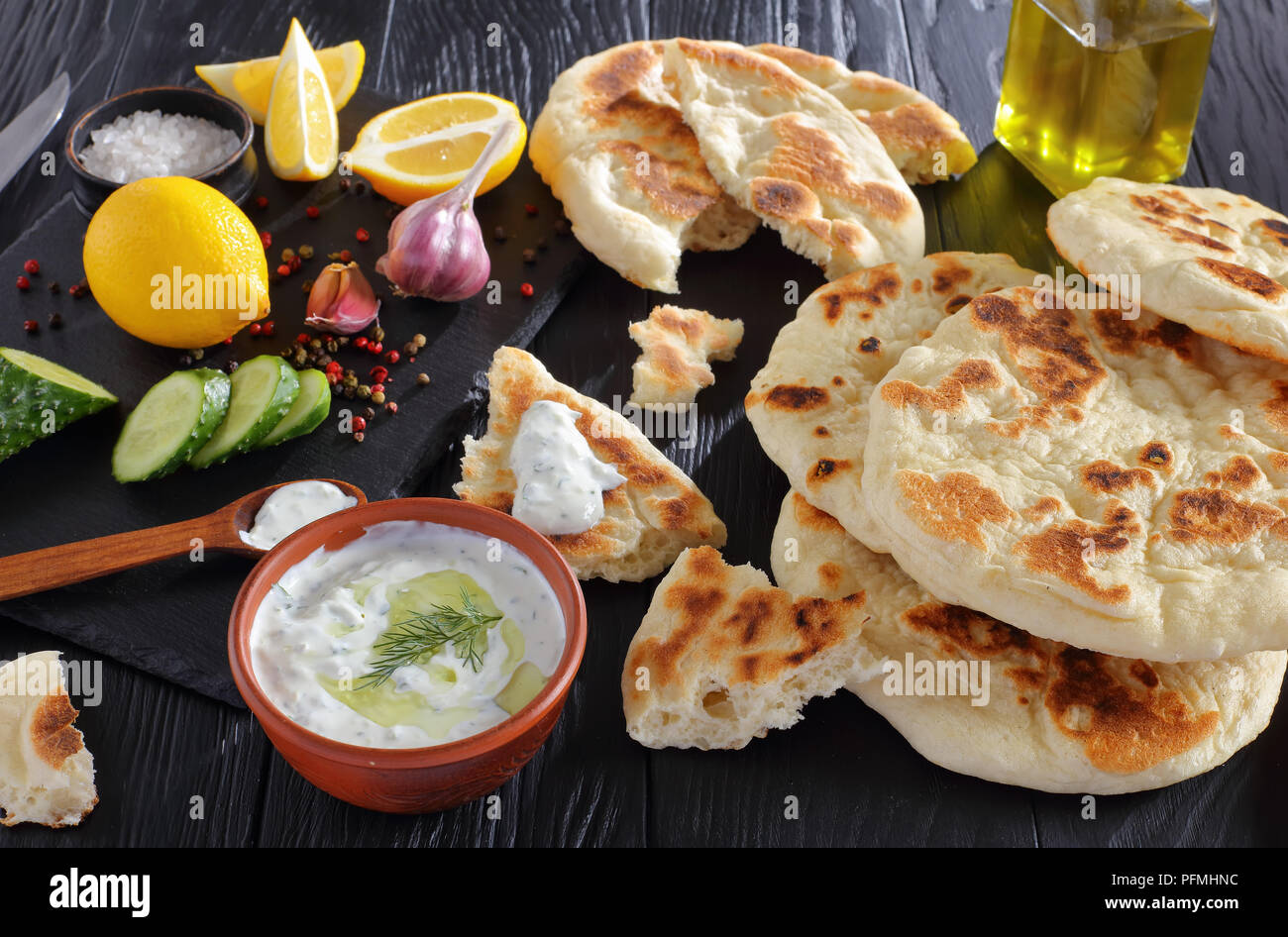 Pane appena sfornato pane pita su tavoli in legno nero con saporita salsa tzatziki. ingredienti sul taglio della pietra bordo, vista orizzontale dal di sopra, close-up Foto Stock