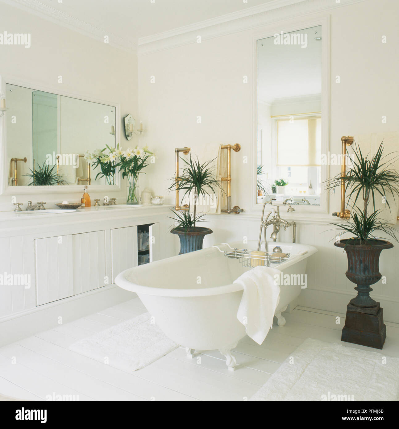 Bagno bianco con stand-alone di vasca da bagno accanto a dotati di unità e di specchi, piante in urne cinerarie Foto Stock