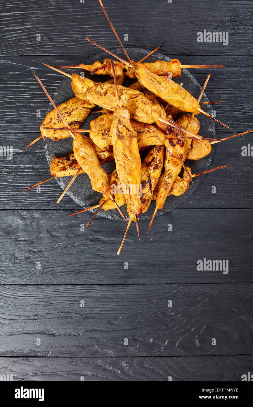 Pollo satay su spiedini su una pietra nera il vassoio su un tavolo di legno, verticale vista da sopra Foto Stock