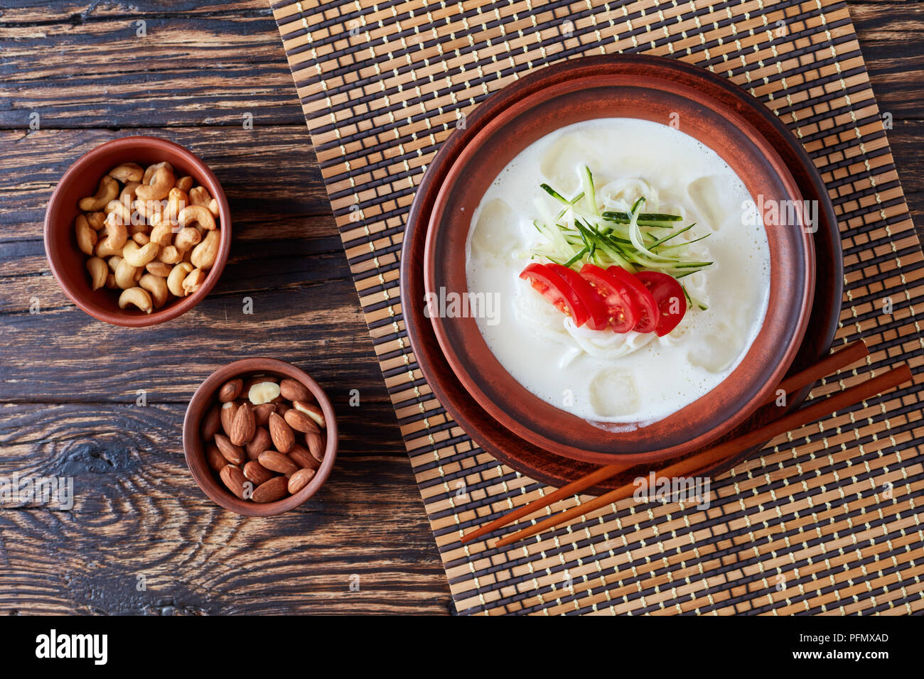 La soia e i dadi latte zuppa coreana kongguksu, Kong-guksu con riso noodle, strisce di cetriolo e le fette di pomodoro in un vaso di argilla con ingredienti su un vecchio woo Foto Stock