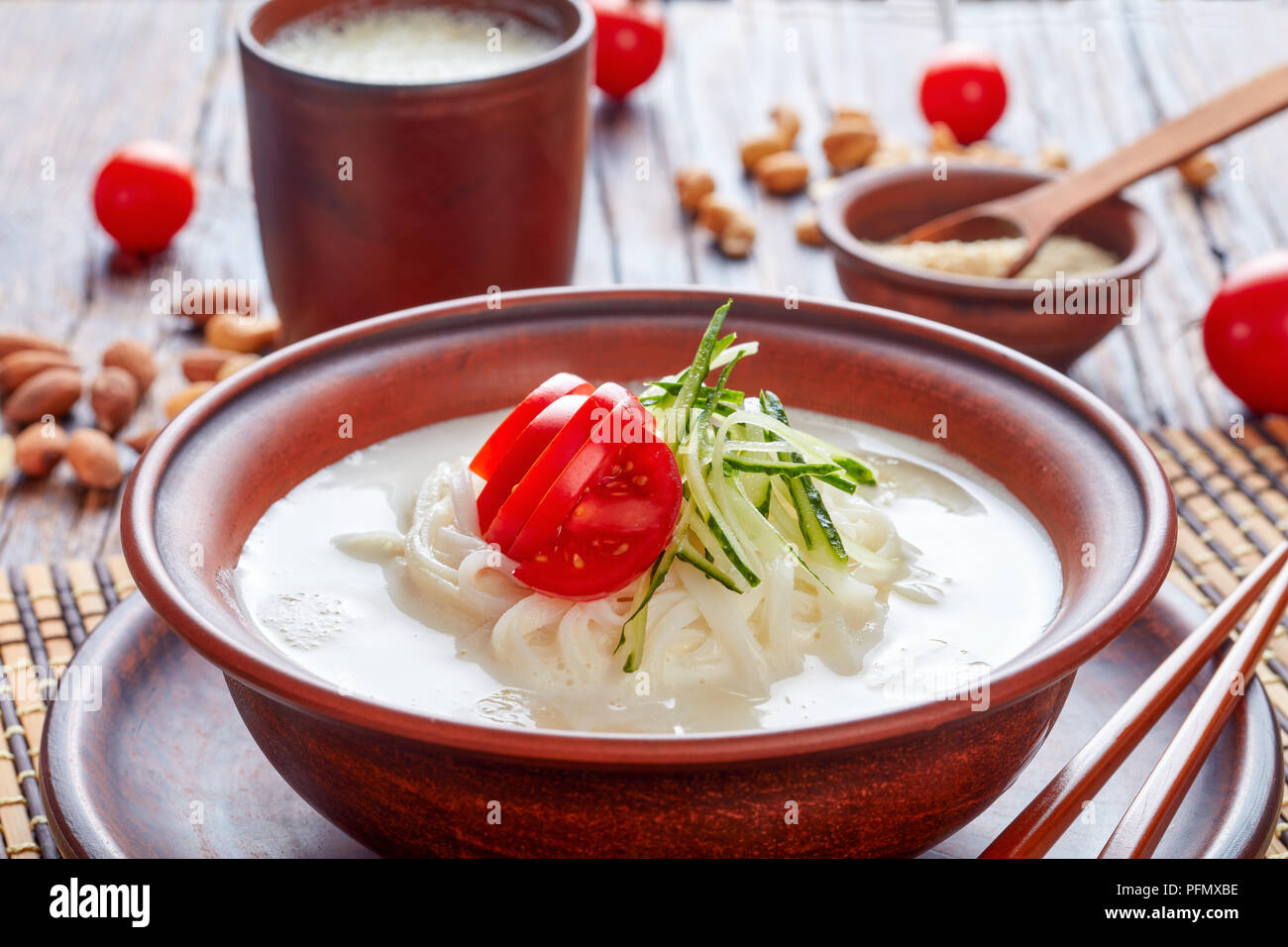 Latte di soia zuppa coreana kongguksu, Kong-guksu con riso noodle, dadi e di sesamo e rabboccato con strisce di cetriolo e le fette di pomodoro in un vaso di argilla con ingred Foto Stock
