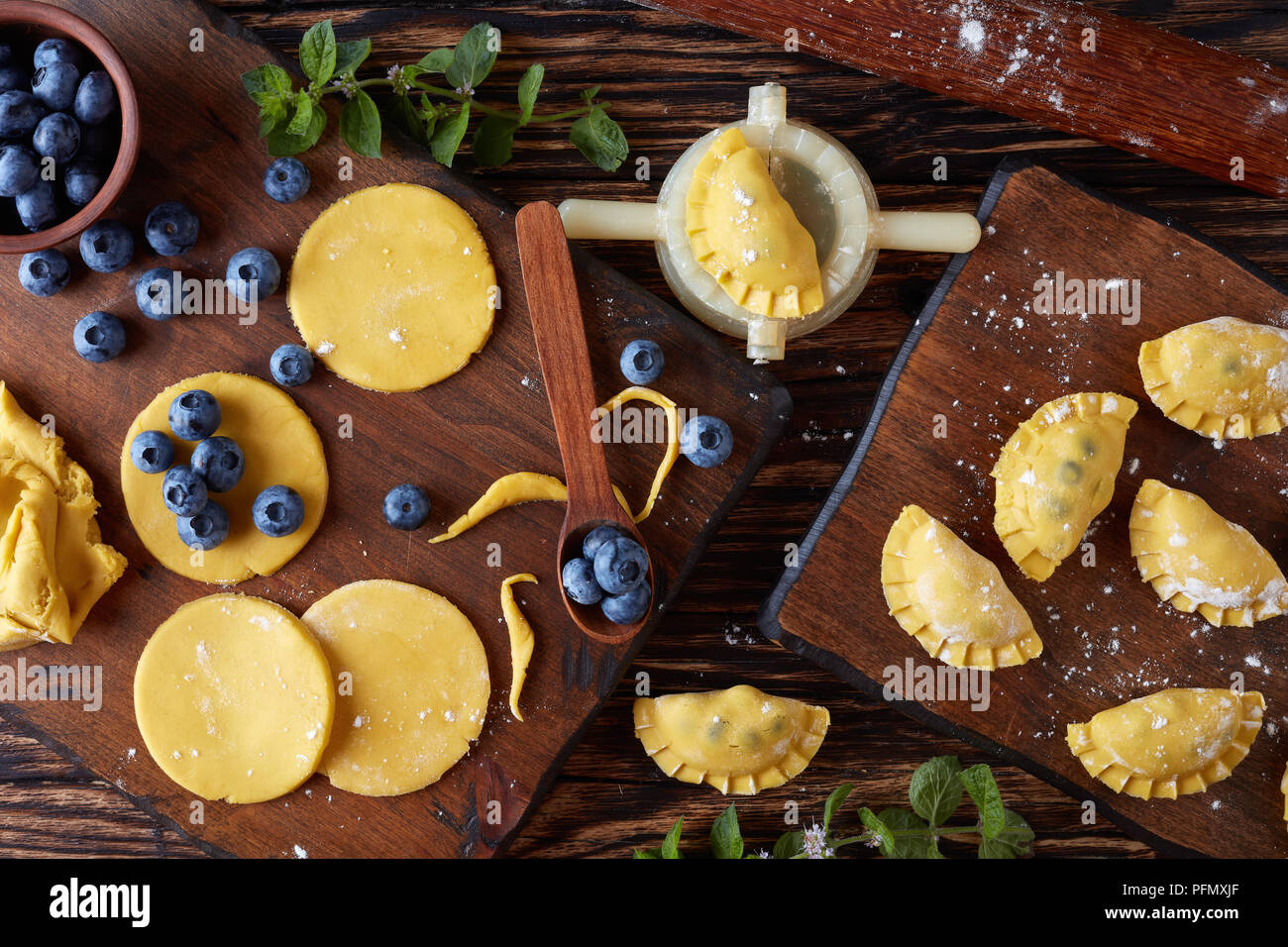 La cottura fino deliziosi gnocchi, pierogi, vareniki con mirtillo ripieni passo-passo. di pasta, gnocco crudo, uno stampo e perno di rotolamento su una oscura rus Foto Stock