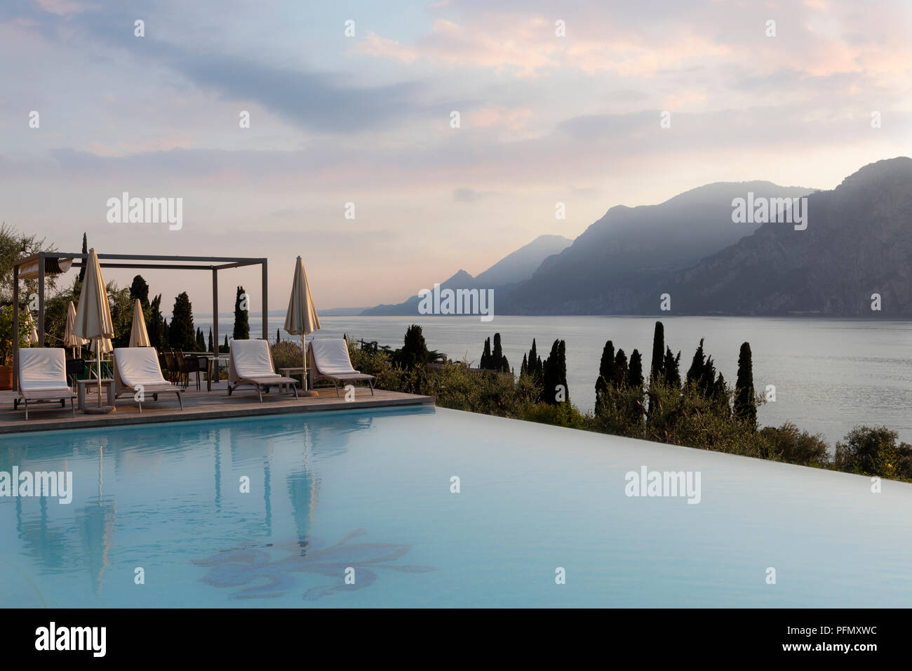 Piscina esterna in hotel di lusso al tramonto con il lago e le montagne Foto Stock