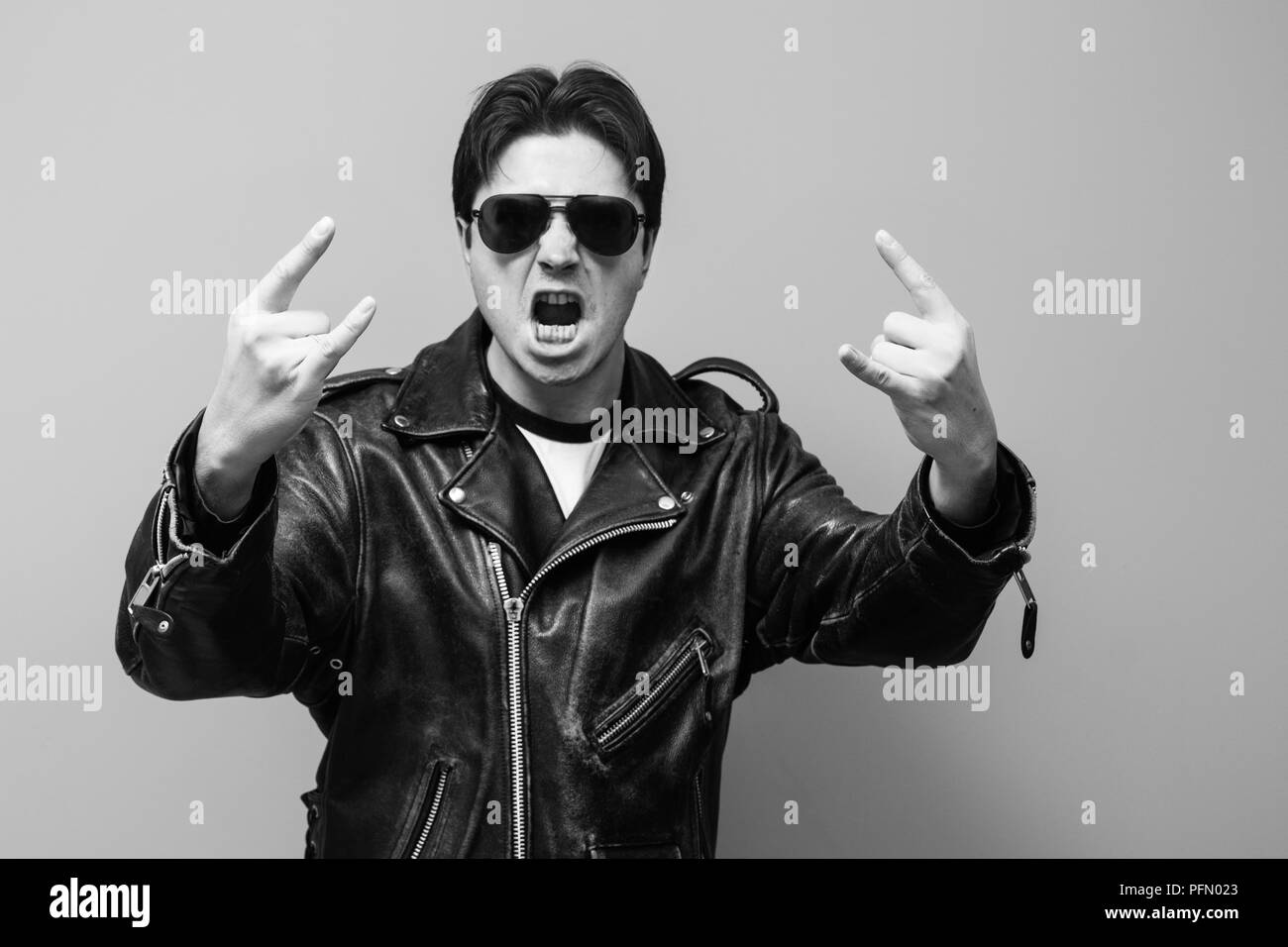 Foto in bianco e nero di un uomo che indossa balck leather biker jacket urla e mostra il segno di corno, tradizionale cultura rock gesto Foto Stock