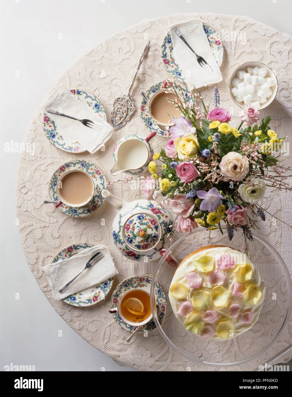 Una tabella set per il tè del pomeriggio, tazze di tè, teiera, piatti e posate, di fiori e di una torta decorata con petali, vista da sopra Foto Stock