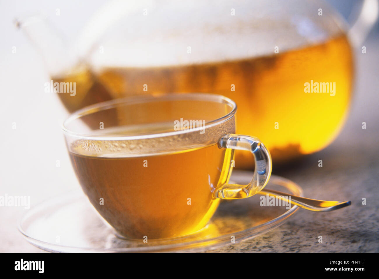 Bicchiere in vetro con piattino contenente tè, vetro teiera in background Foto Stock