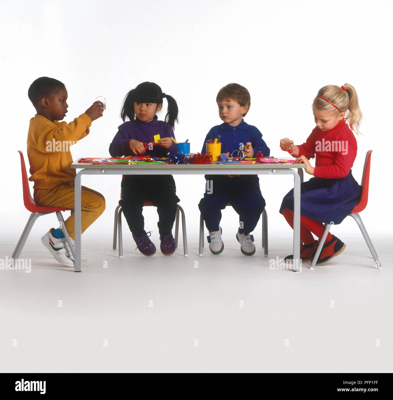 Quattro bambini seduti a tavola rendendo le maschere di carta Foto Stock