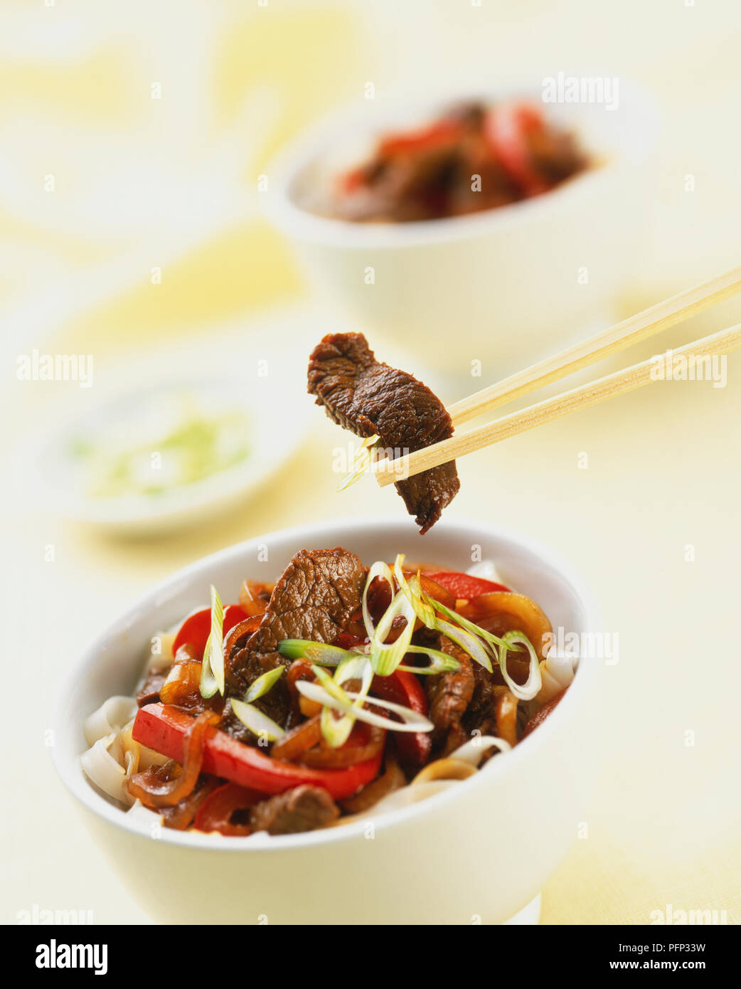 Striscia di stir-fried carni bovine detenute fino con bacchette sopra un piccolo recipiente contenente la carne e le verdure rosolare, vicino. Foto Stock