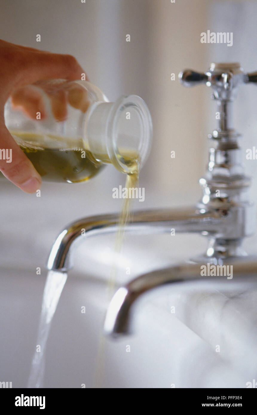 Versando olio da bagno in vasca di acqua dai rubinetti, movimento sfocato Foto Stock