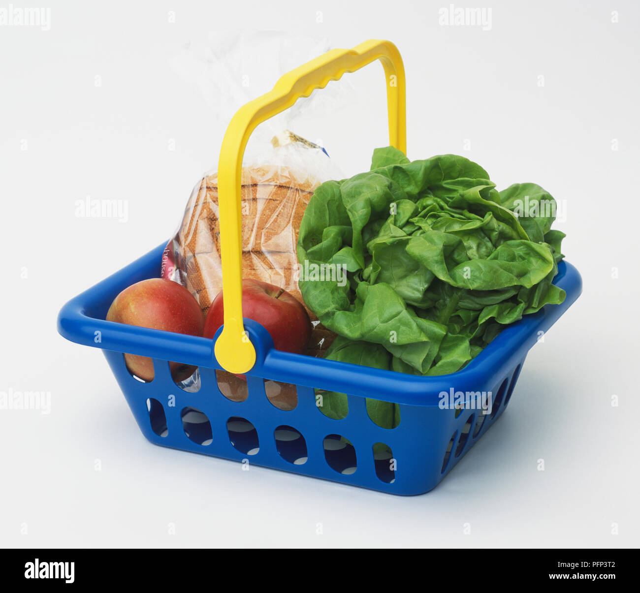 Cestello blu con manico di colore giallo, contenente le mele rosse, fette di pane avvolto in plastica e testa di lattuga. Foto Stock