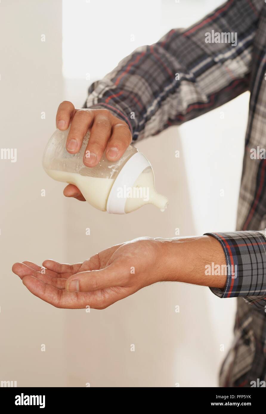 L'uomo prova la temperatura del latte nel biberon, close-up Foto Stock