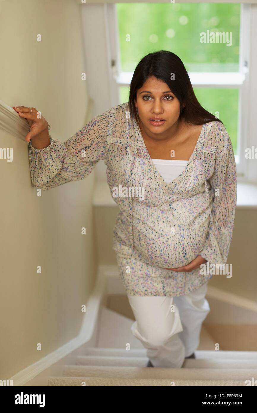 Donna incinta salendo le scale di tenere su ringhiere, vista frontale Foto Stock