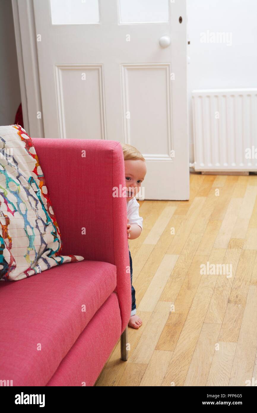 1 anno di età baby boy peeking intorno al lato del divano Foto Stock