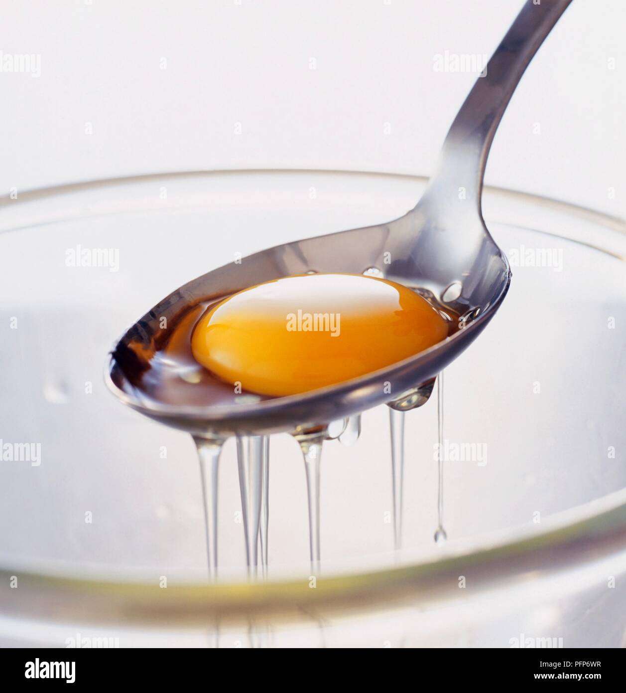 Tuorlo d'uovo nel mestolo forato essendo separato dal bianco, close-up Foto Stock