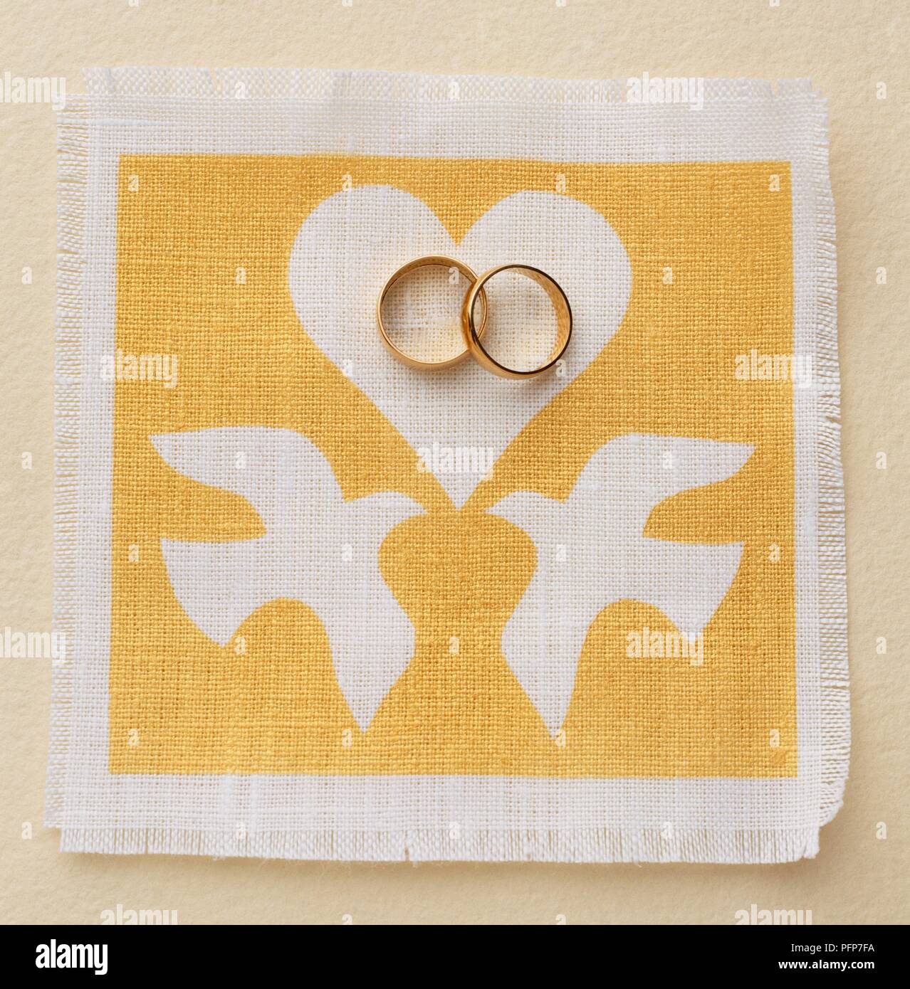 Oro anelli di nozze su giallo tessuto decorato con cuore bianco e colombe Foto Stock