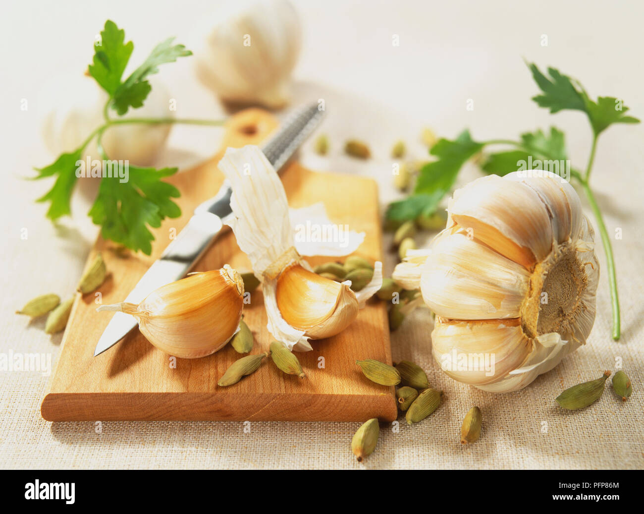 Allium sativum, aglio, capi e chiodi di garofano, Elettaria cardamomum, cardamomo, baccelli sul tagliere di legno con il reticolo coltello, concentrarsi sul primo piano. Foto Stock