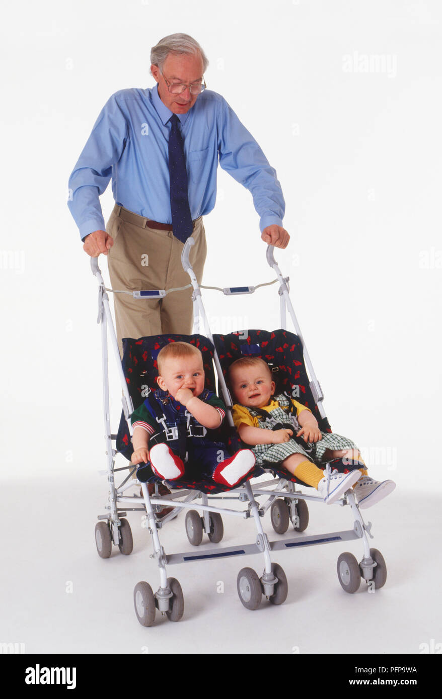 Uomo con i capelli grigi a spingere un passeggino doppio con due bimbi in Foto Stock