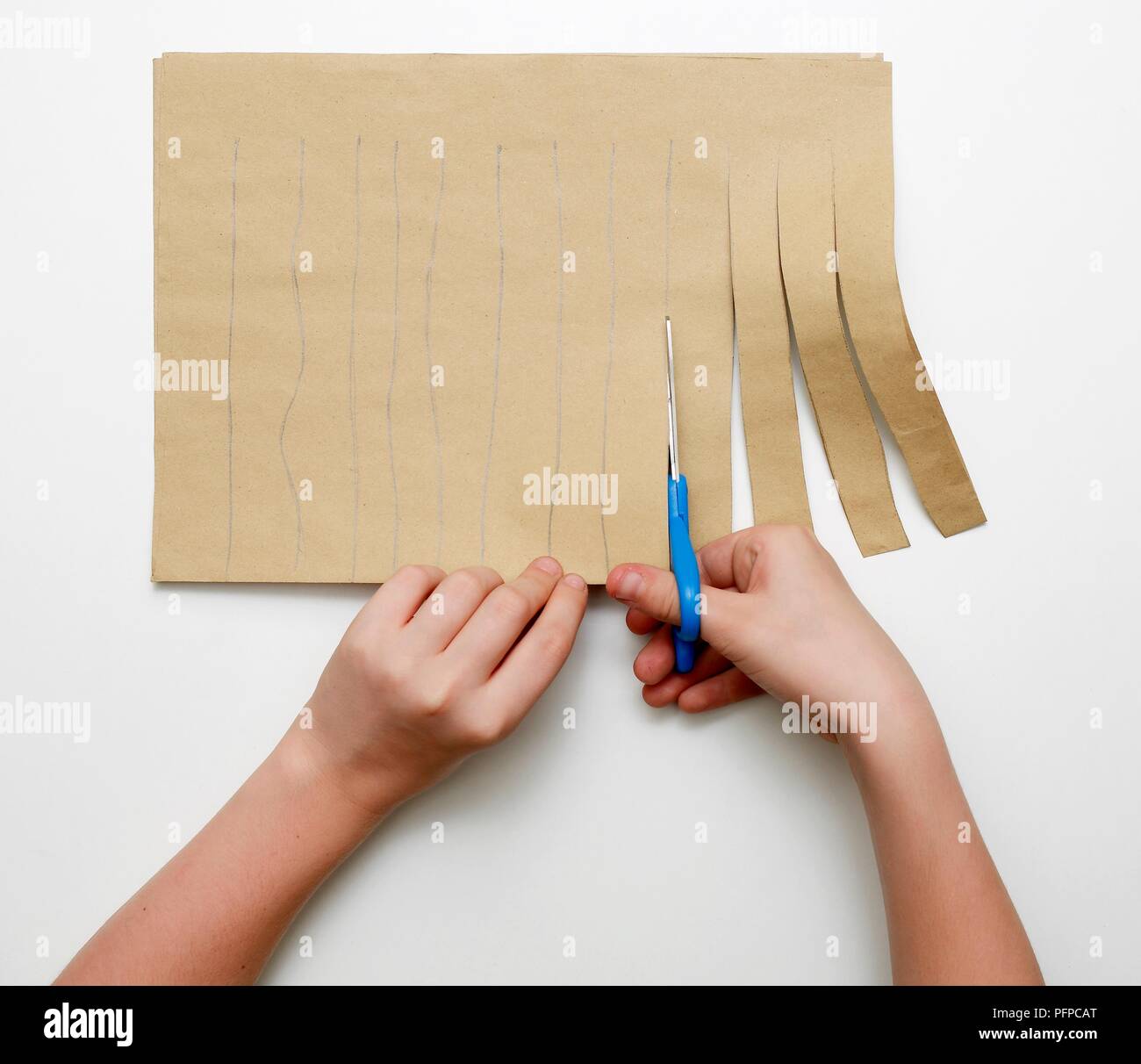 Ragazza con le mani in mano il taglio di carta marrone in strisce lungo le linee tracciate con la matita, close-up Foto Stock