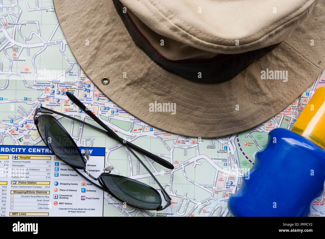 Cappello, occhiali da sole, crema solare e mappa Foto Stock