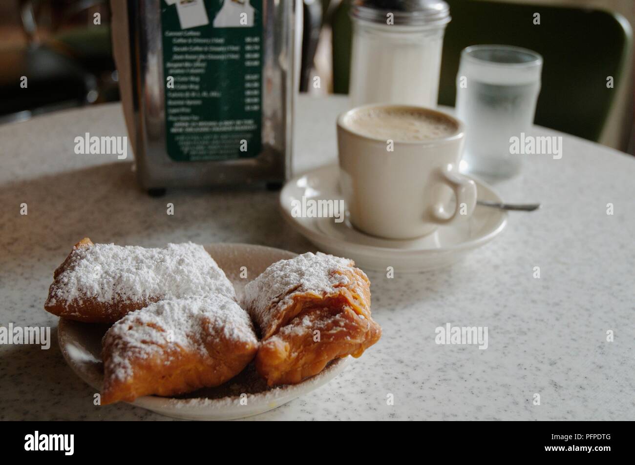 Stati Uniti d'America, Louisiana, New Orleans, Cafe du Monde, una tazza di caffè espresso accanto alla glassa di zucchero-spolverata di pasticceria su un tavolo Foto Stock