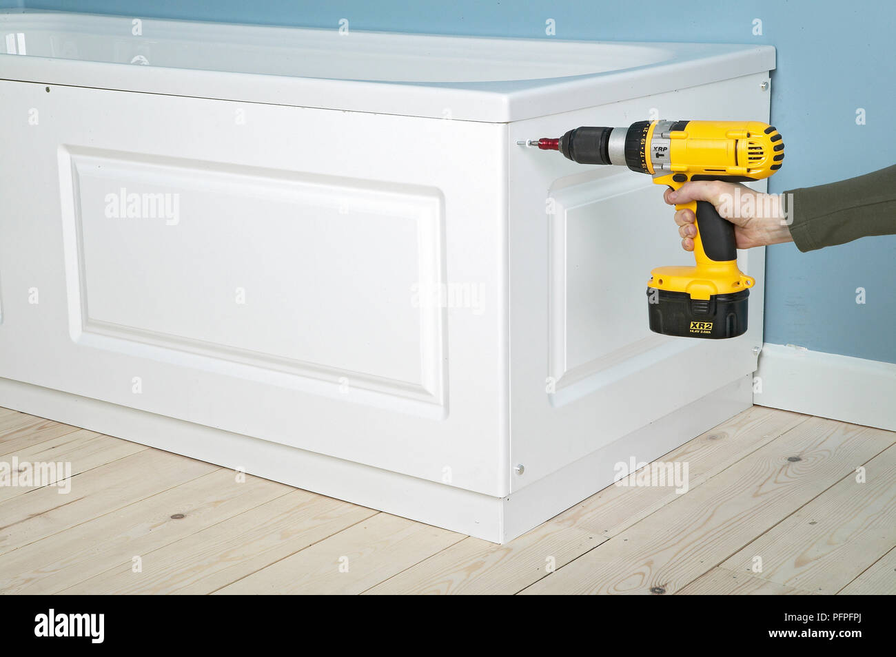 Uomo di potenza utilizzando un cacciavite per fissare il pannello al telaio che circonda il bagno Foto Stock