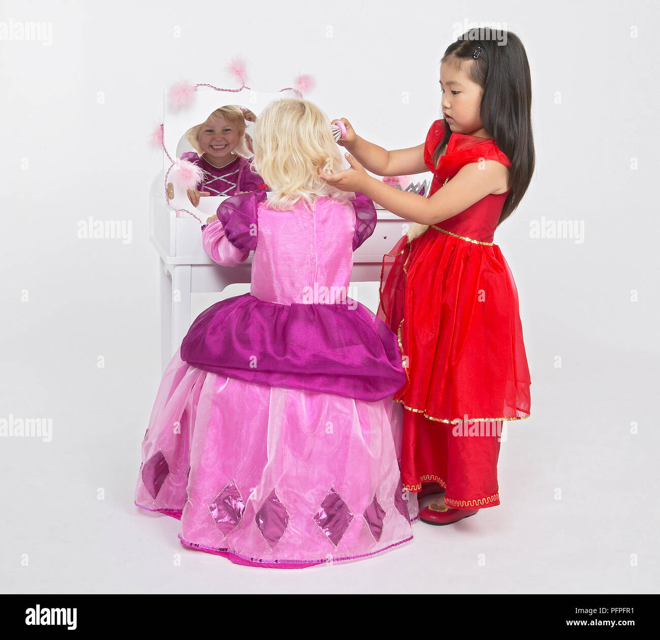 Ragazza in rosa principessa abito su una sedia di fronte bianca di toeletta, ragazza in abito rosso spazzolare i capelli Foto Stock