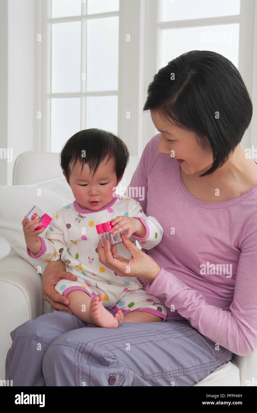 La madre tiene il bambino sul suo grembo, baby giocando con due dei giocattoli di plastica Foto Stock