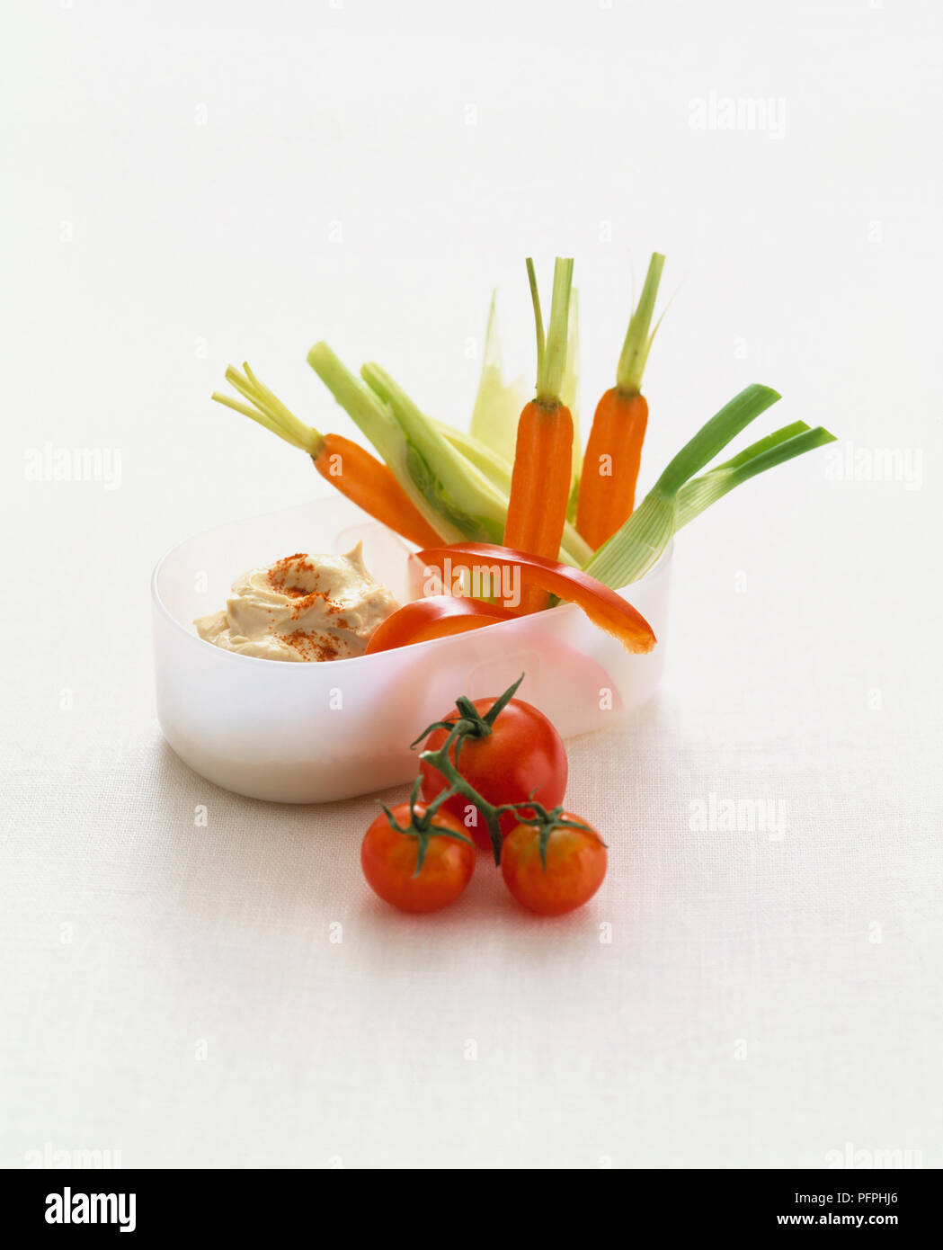 I pomodori tagliati a fette di carote, cipolline, il peperone rosso e humus in contenitore di plastica Foto Stock