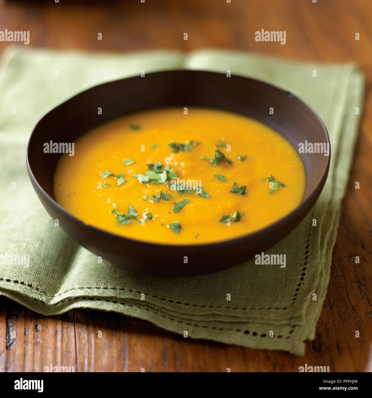 La carota e la zuppa di arancia guarnito con coriandolo servito in tazza marrone sul tovagliolo verde, close-up Foto Stock