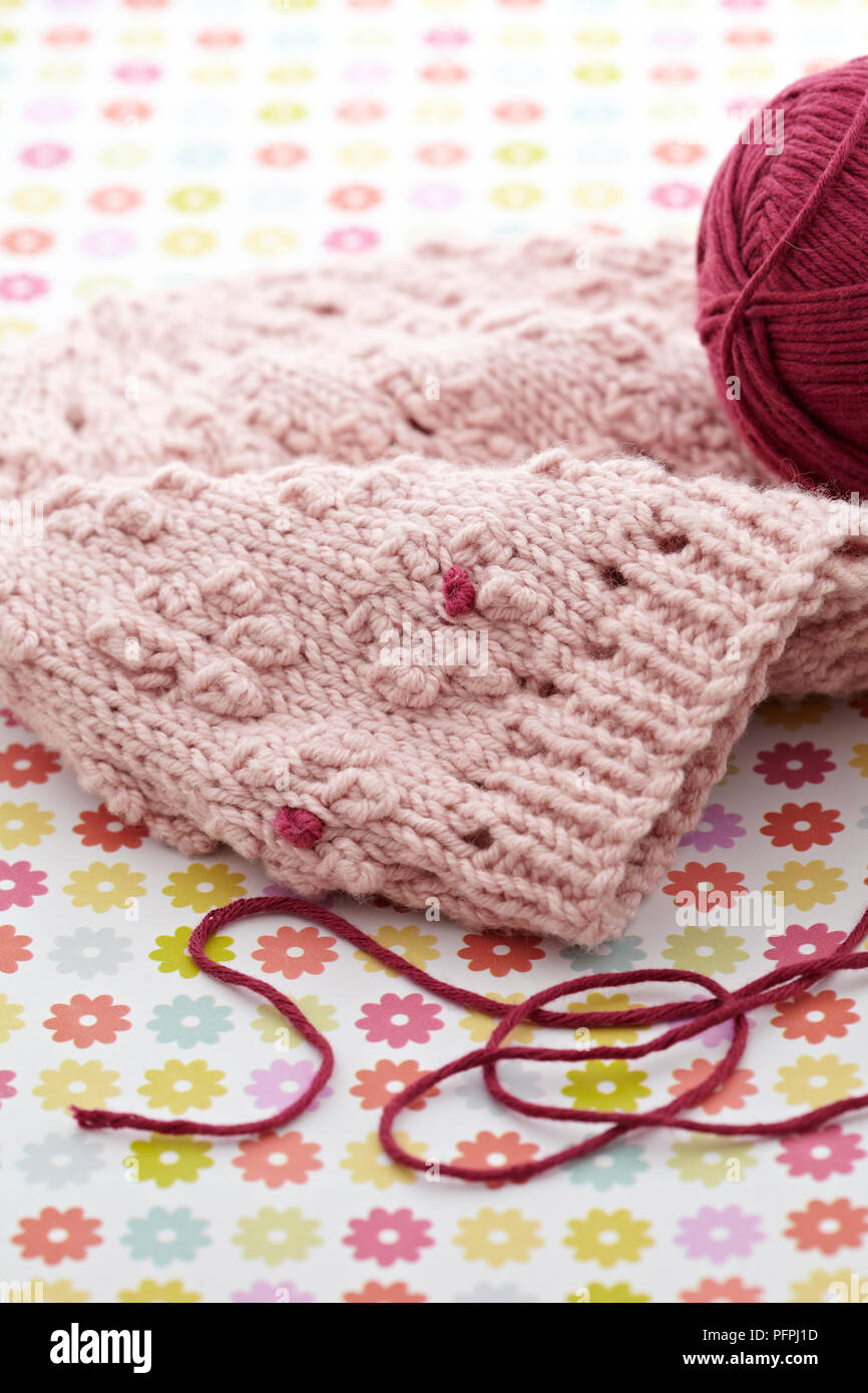 Fiore rosa-modellato beanie hat con sfera di lana su sfondo floreale Foto Stock