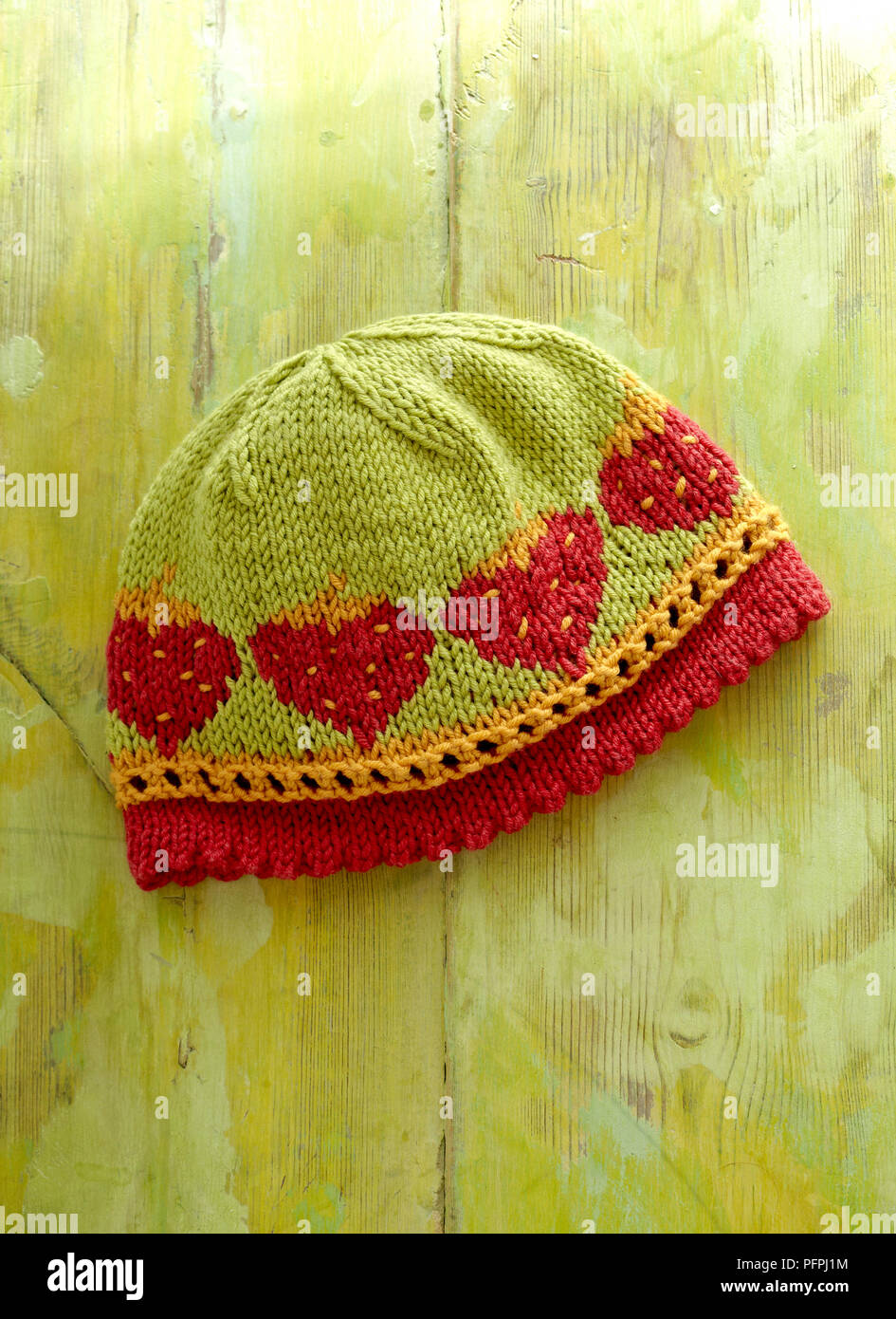 Fragola con fantasie di bambino in maglia del cappello verde su uno sfondo di legno Foto Stock