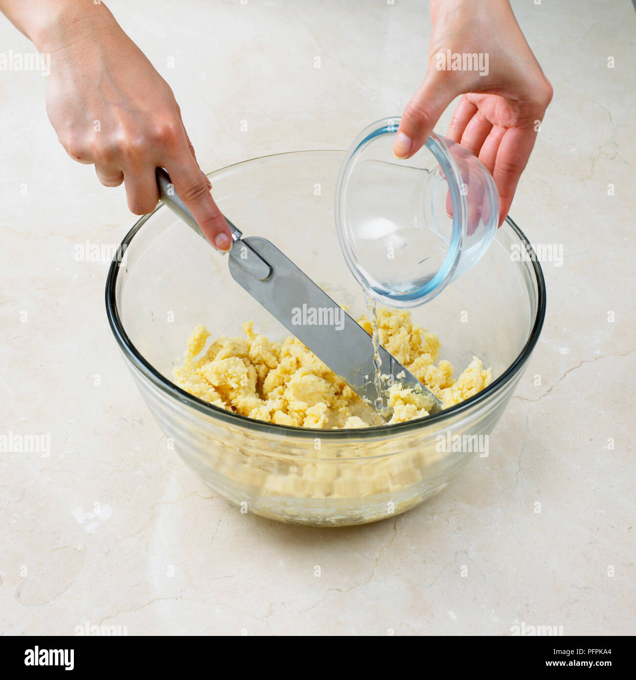 L'aggiunta di acqua fredda per pasta frolla miscela nel recipiente e miscelazione in con una spatola Foto Stock