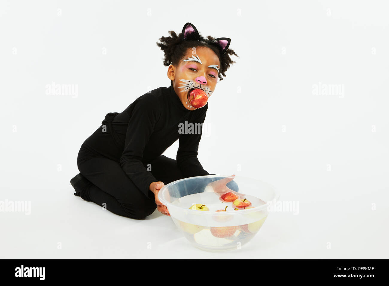 Ragazza vestita come un gatto nero con una ciotola di mele Foto Stock