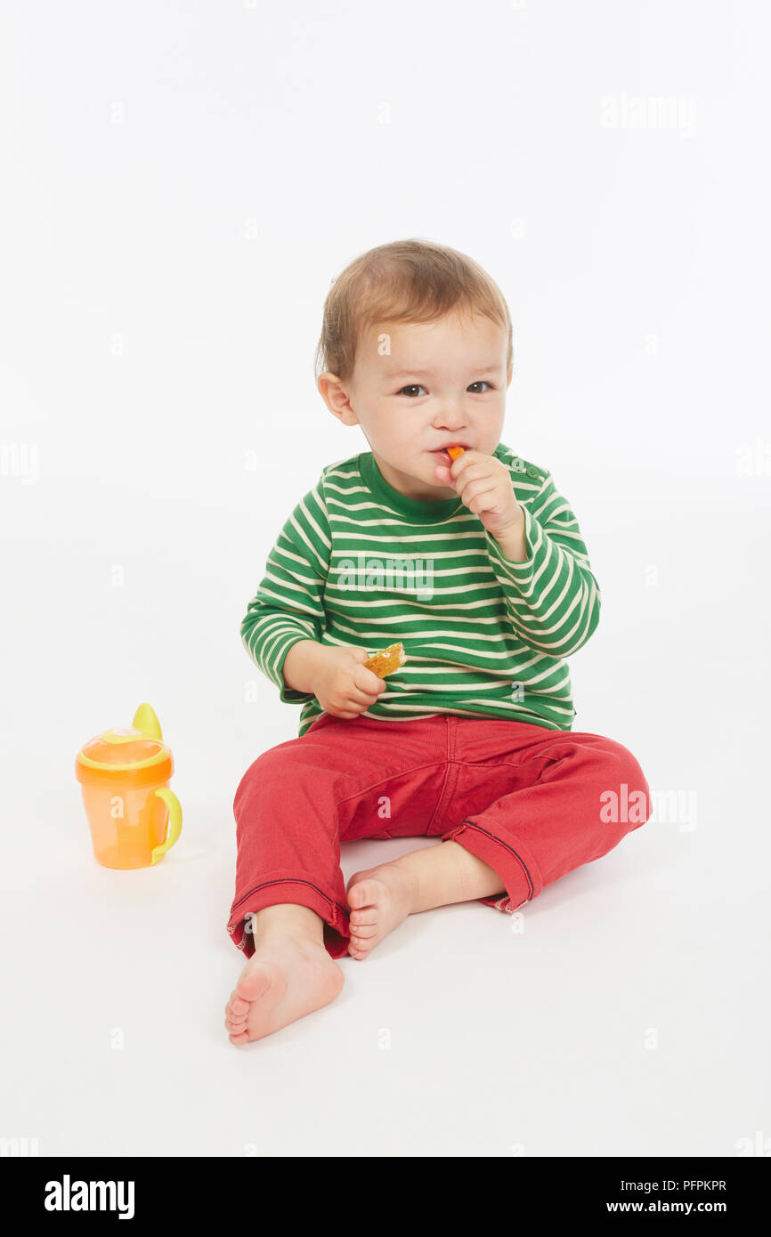 Little Boy in verde stripey top mangiare una carota stick (Modello età - 22 mesi) Foto Stock