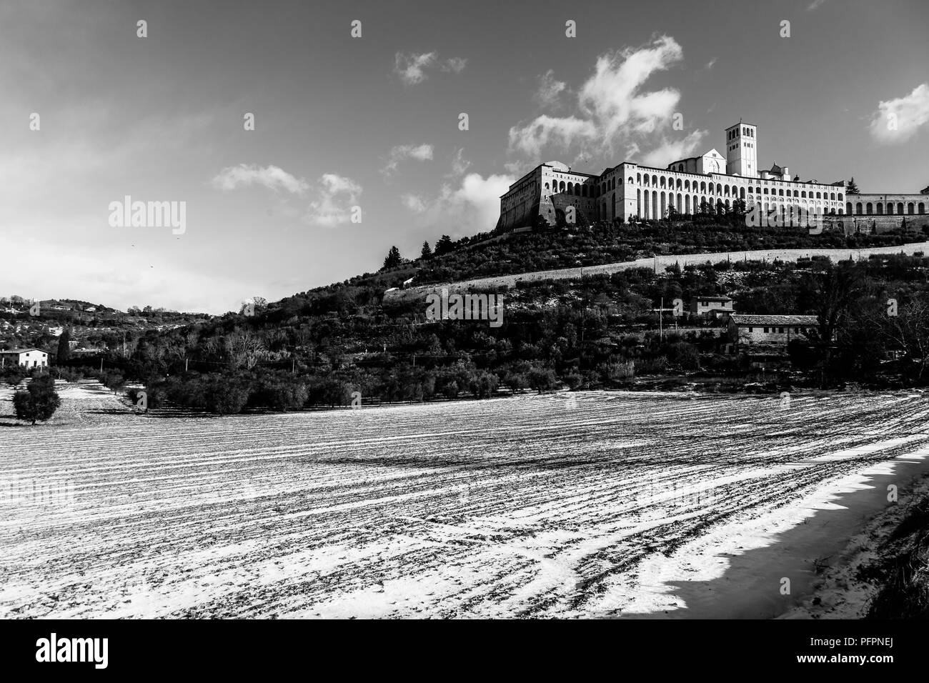 Vista della città di Assisi (Umbria) in inverno, con un campo coperto di neve e cielo con nuvole bianche Foto Stock