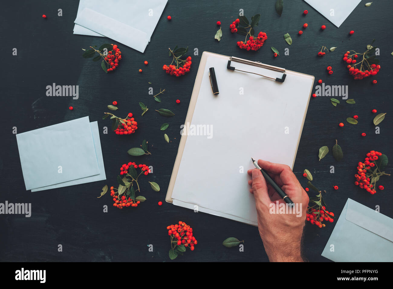 Piatto stendere la mano scrivere lettera su appunti notepad e busta, vista dall'alto mock up copia spazio per la scrittura di lettere su sfondo scuro decorata con Foto Stock