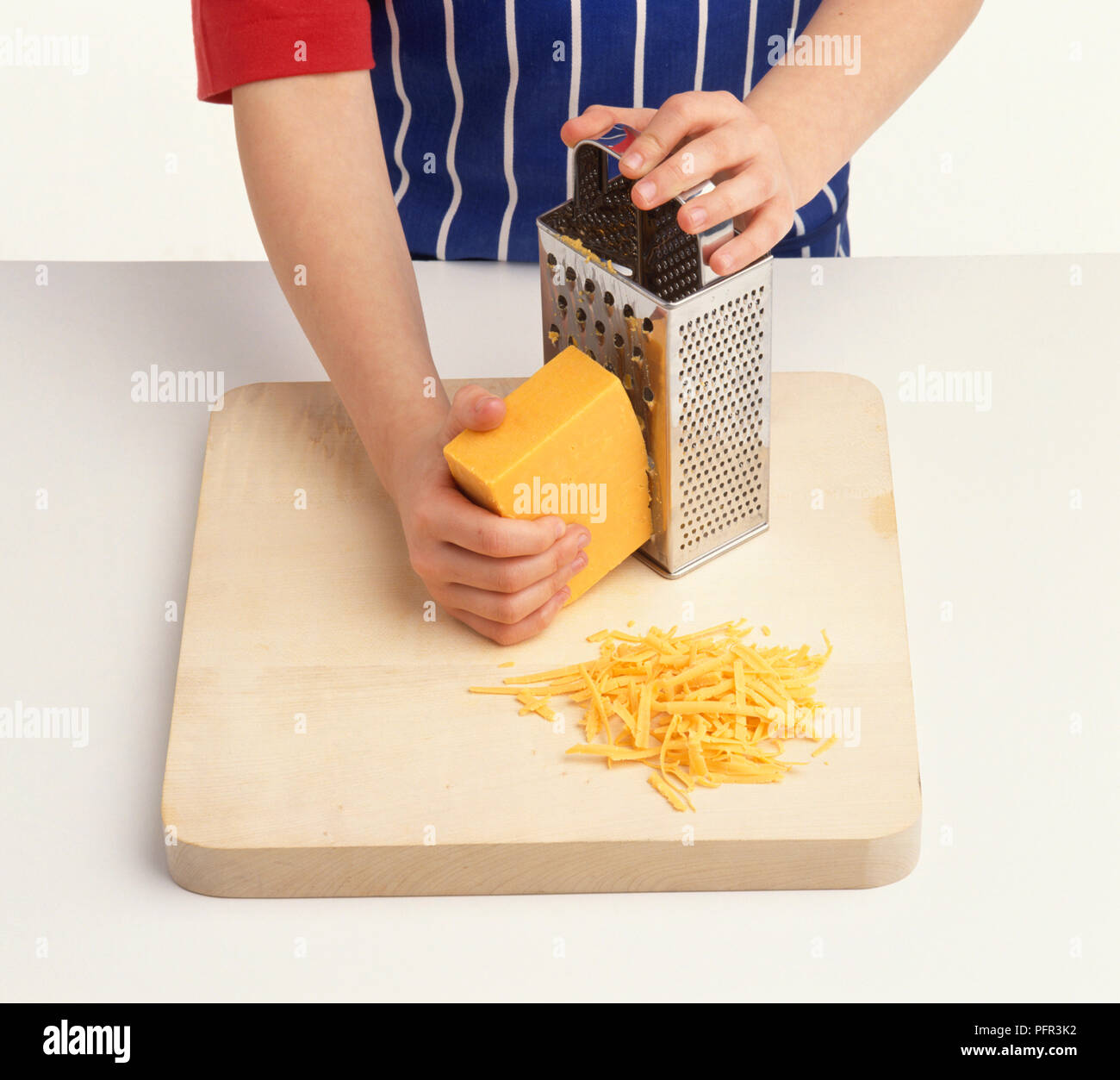 Bambino grattugiare il formaggio sul tagliere Foto Stock