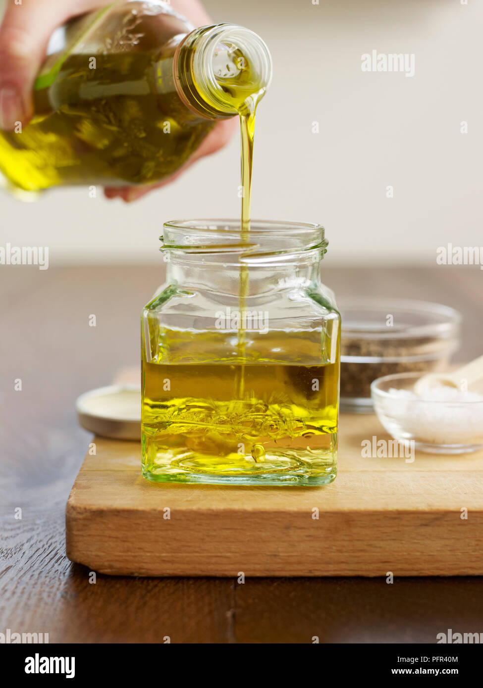 Versando l'olio d'oliva in vaso piccolo contenente aceto di vino bianco (rendendo la vinaigrette) Foto Stock