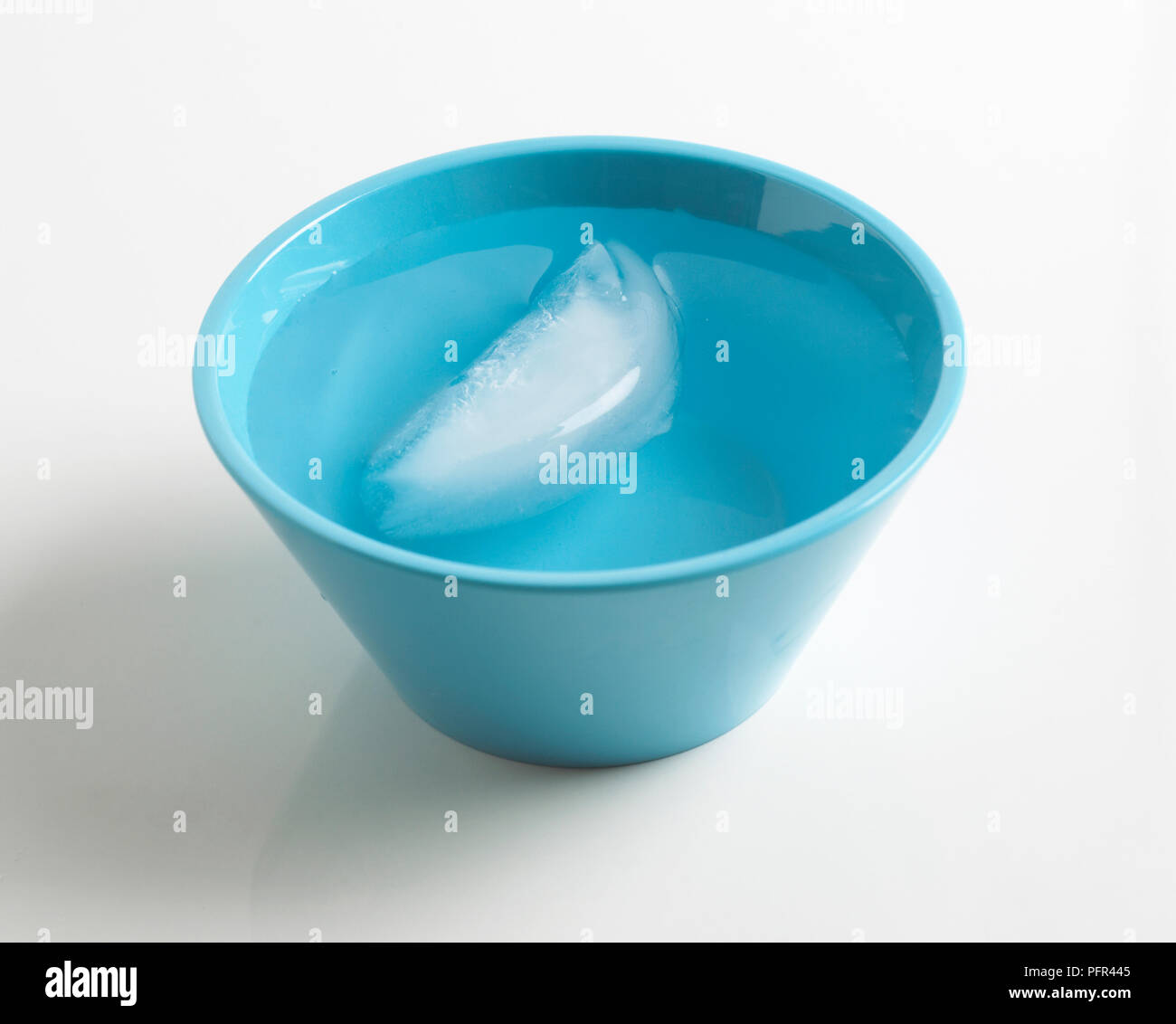 Il cubo di ghiaccio galleggiante nella ciotola blu di acqua Foto Stock