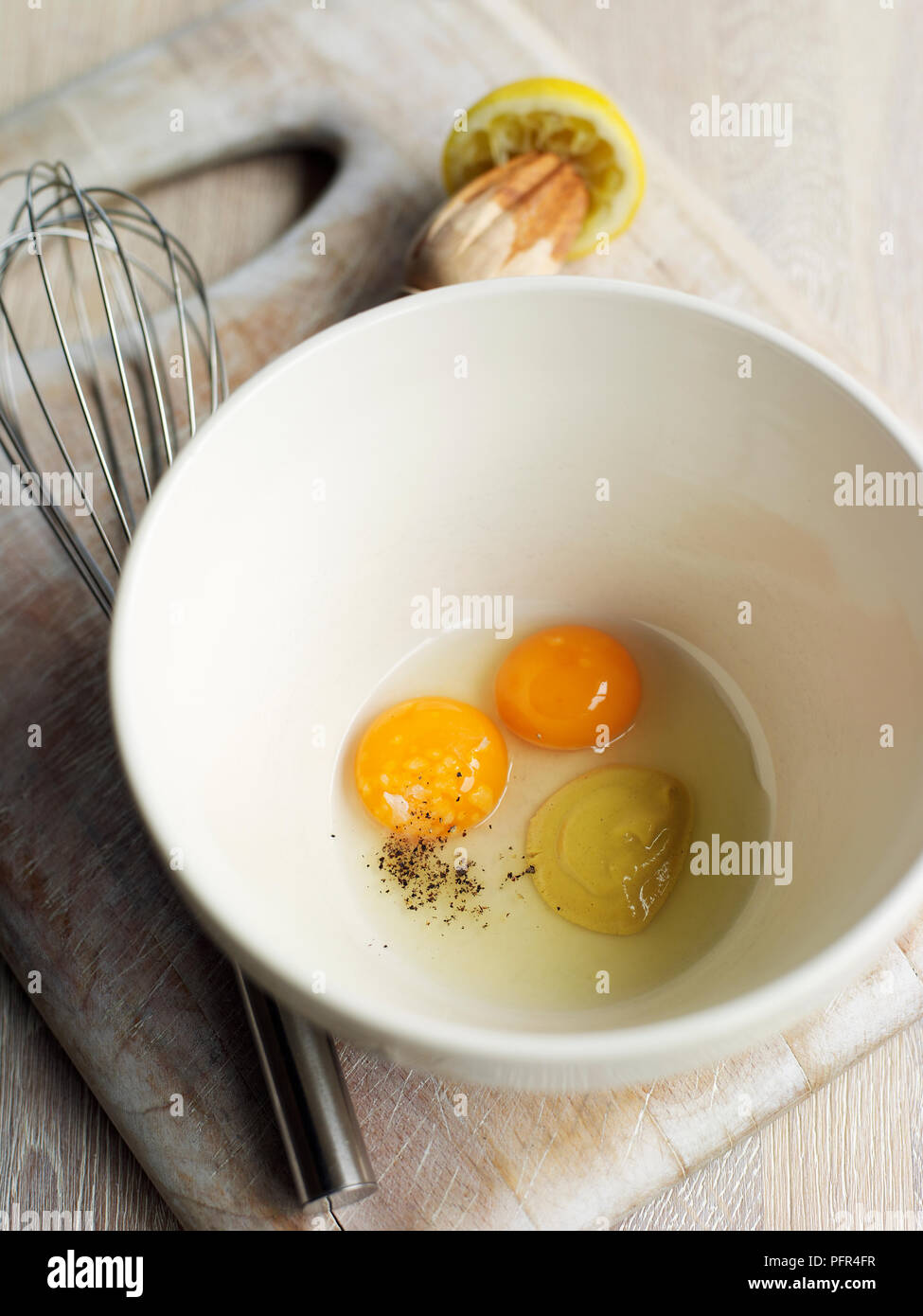 Uova, la senape e il succo di limone in un recipiente, frusta nelle vicinanze (ingredienti per la maionese) Foto Stock