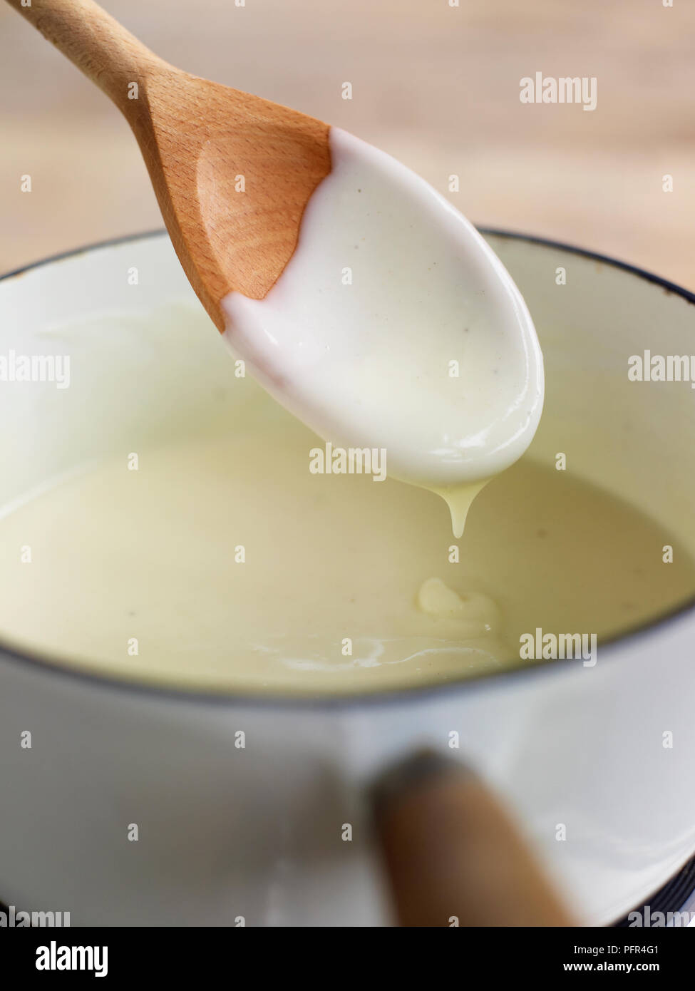 Cuocere la besciamella in casseruola e gocciolamenti dal cucchiaio di legno Foto Stock