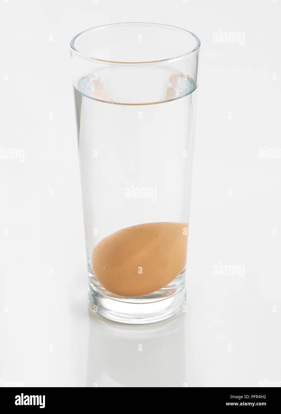 Uovo affondata al fondo di un bicchiere di acqua (lavandino o di flottazione la freschezza delle uova prova) Foto Stock