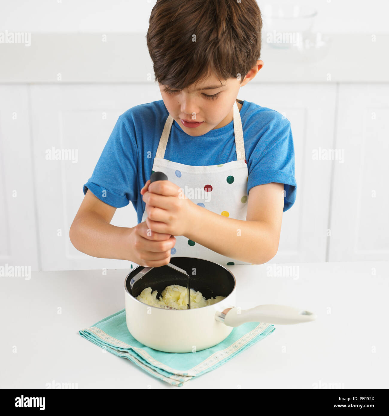 Ragazzo schiacciare le patate in una pentola, 7 anni Foto Stock