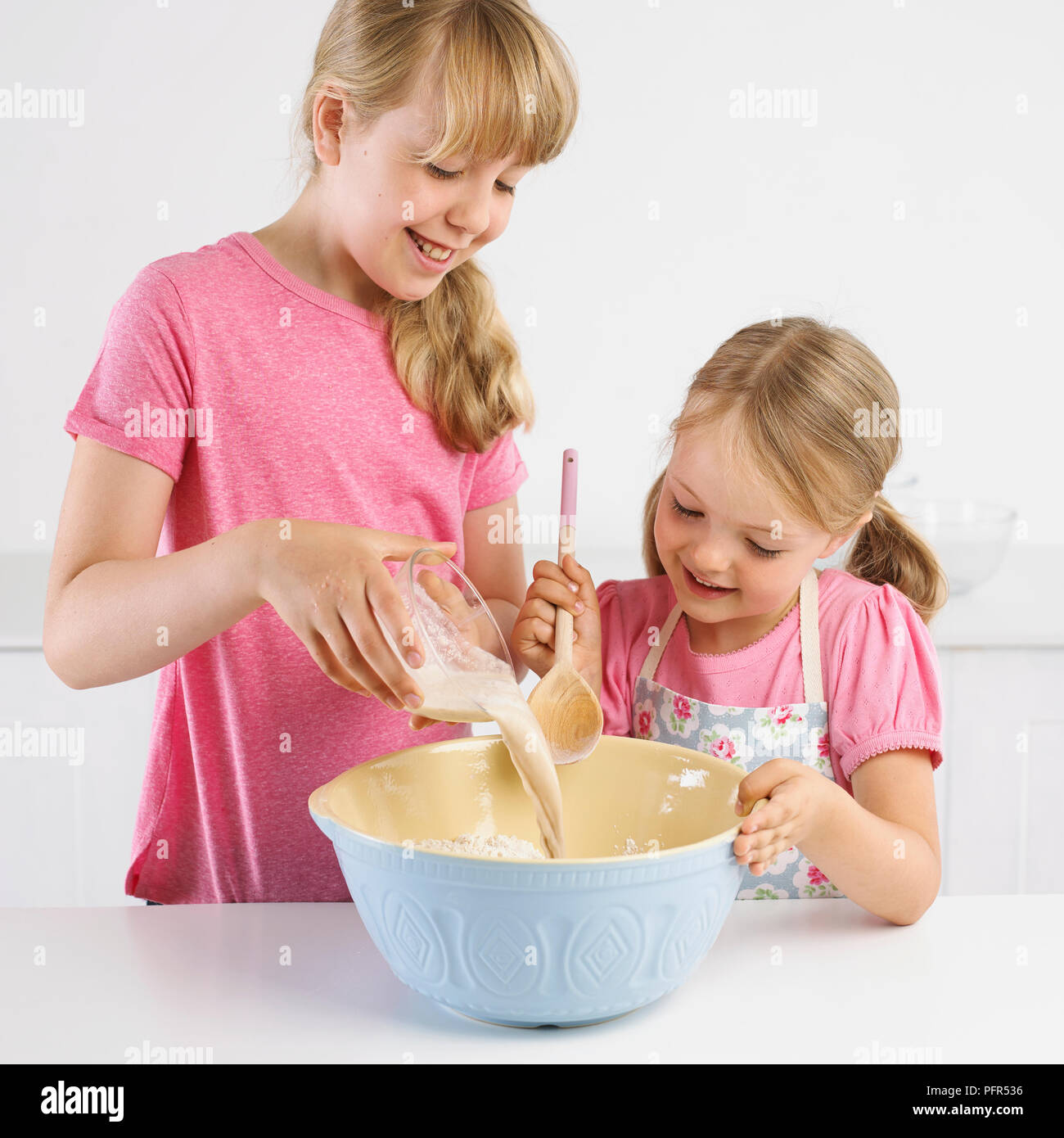 Ragazze versando il lievito e mistura di acqua nella tazza di farina, 5 anni e 9 anni Foto Stock