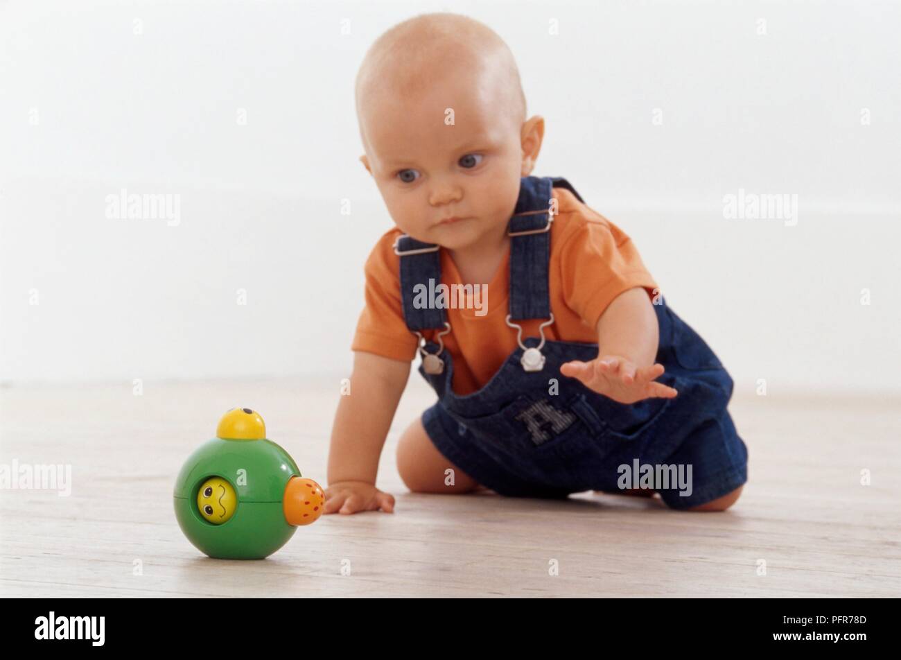 8 mese fa baby boy strisciare sul pavimento verso il giocattolo di plastica Foto Stock
