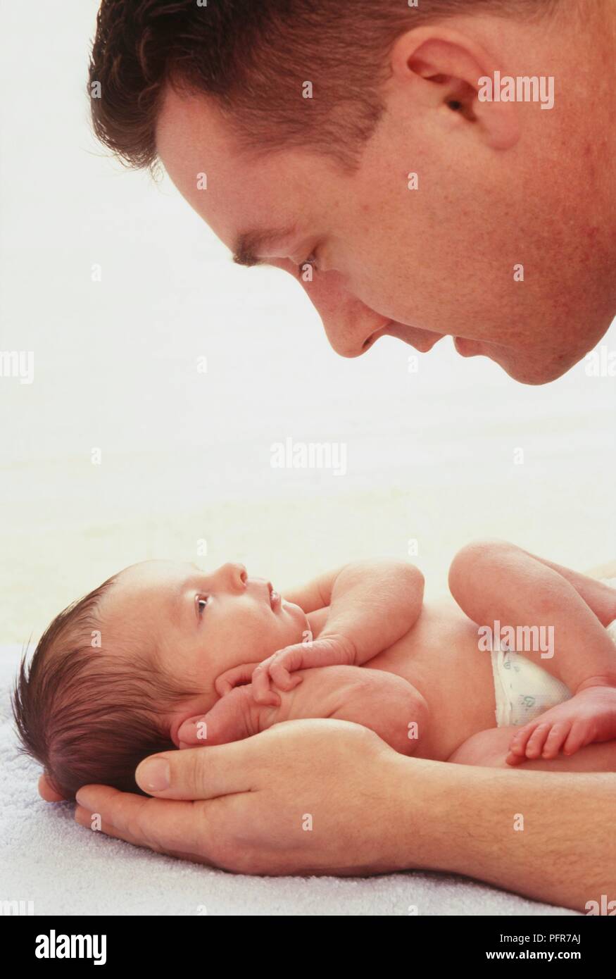 Uomo che guarda oltre il neonato ragazza distesa su un asciugamano close-up, vista laterale Foto Stock